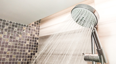 Picture of shower head spraying water in modern bathroom with tiles in the background