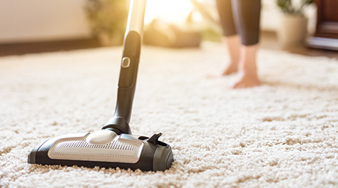 Woman hoovering thick carpet with sun shining through the window