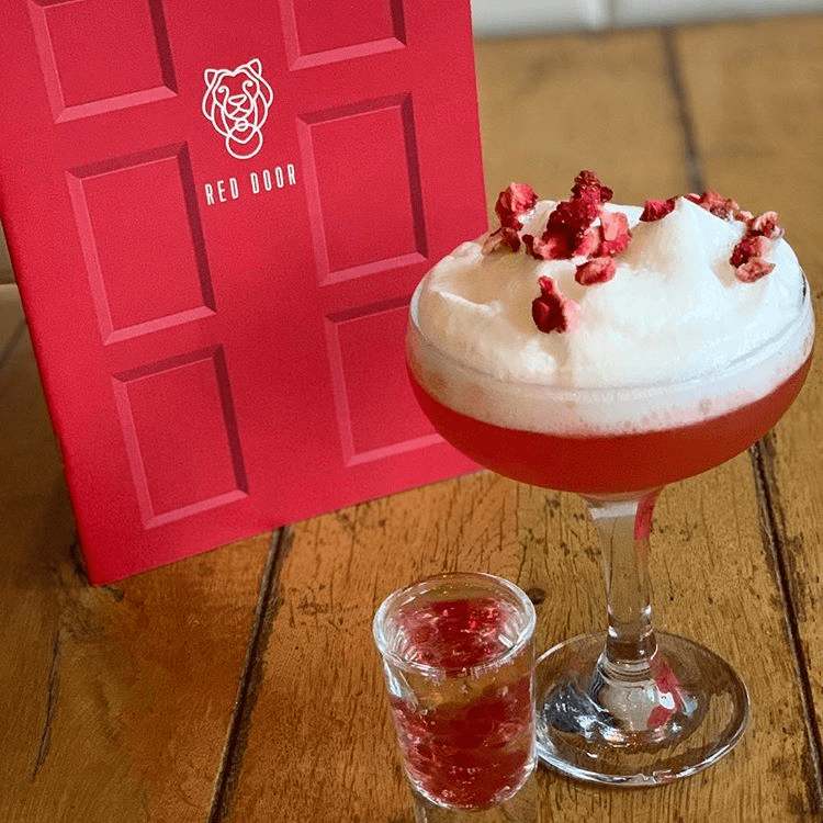 Image taken of delicious looking cocktail from bar Red Door with a red door menu next to it. 