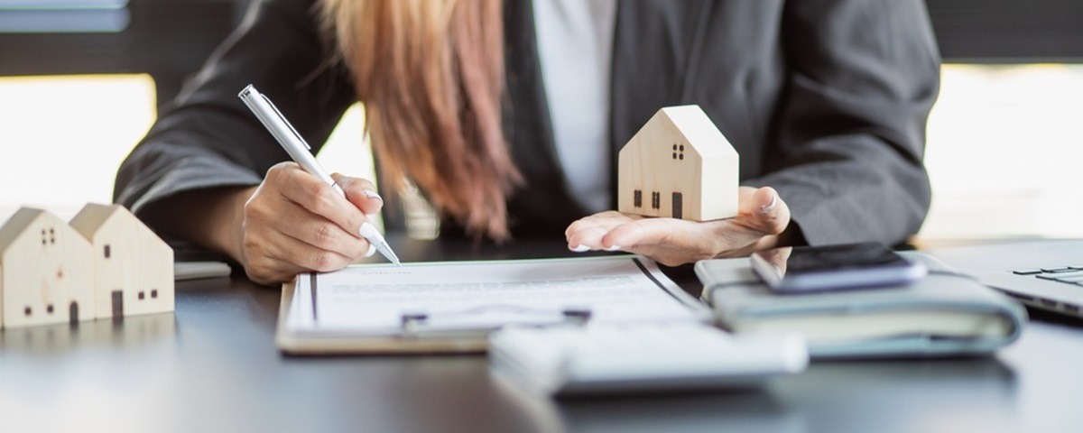 Mortgage advisor holding wooden home and signing documents