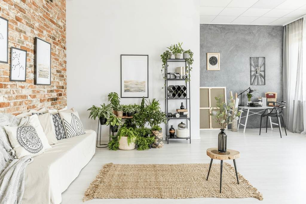 Spacious, well-lit living room with white sofa, brick wall and many house plants. 